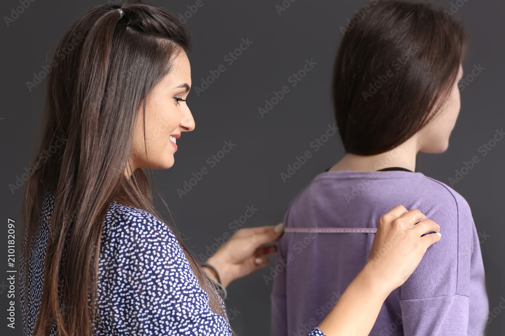 Young female tailor taking clients measurements in atelier
