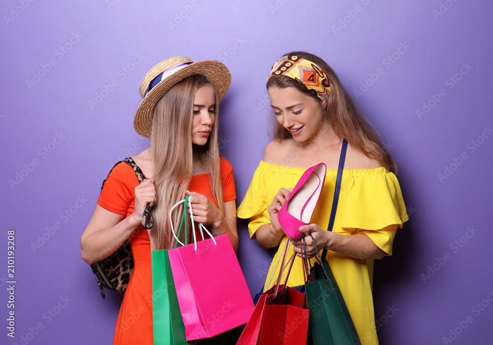 Beautiful young women with new shoes and shopping bags on color background