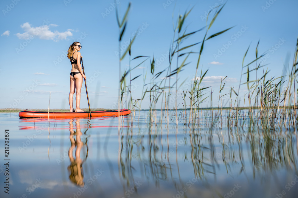黎明时分，一名女子在芦苇和平静的湖面上划船
