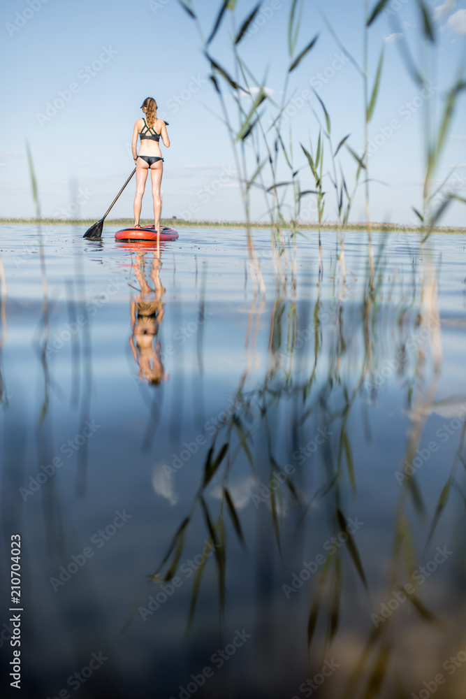 黎明时分，一名女子在芦苇和平静的湖面上划船