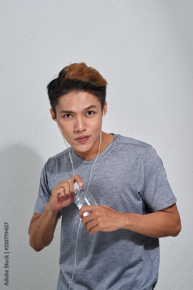 英俊的年轻肌肉运动员拿着一瓶水听音乐