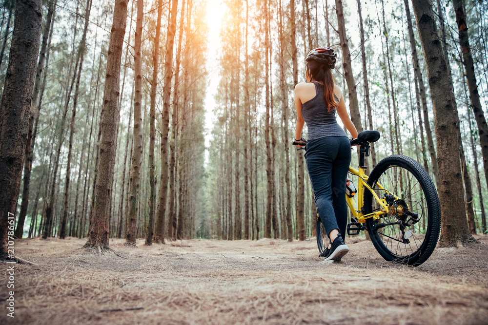 Asian girl is exercising, and riding the bycycle the weekend in a pine forest green and lush beautif