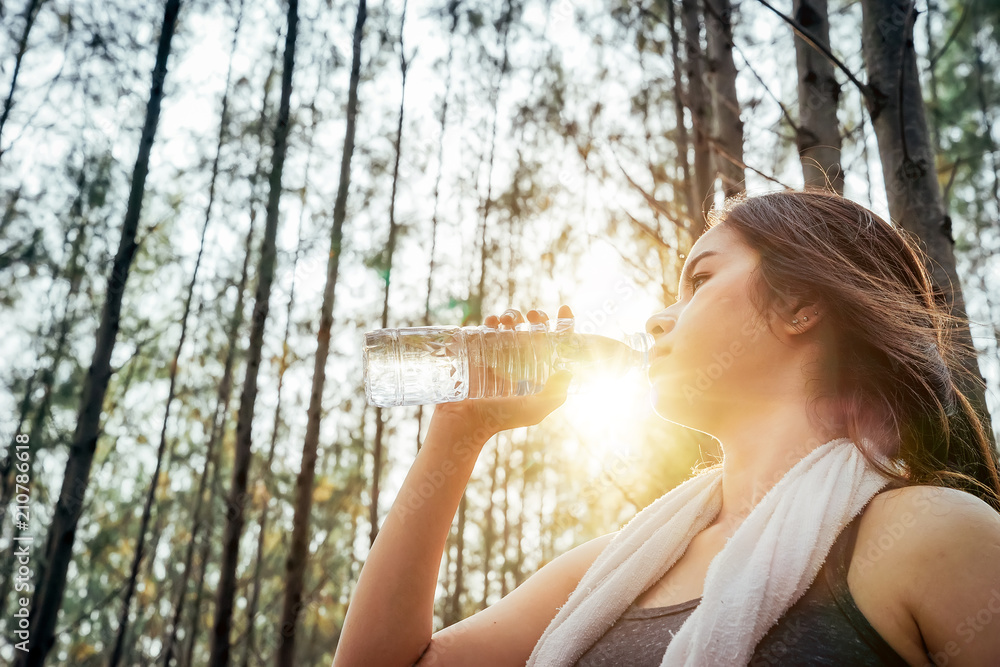 亚洲女孩正在锻炼身体，周末在一片松林里喝清凉的水。
