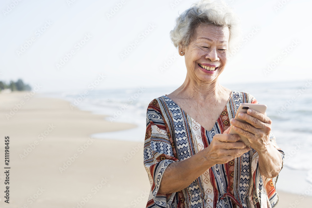 在海滩上使用手机的资深亚洲女性