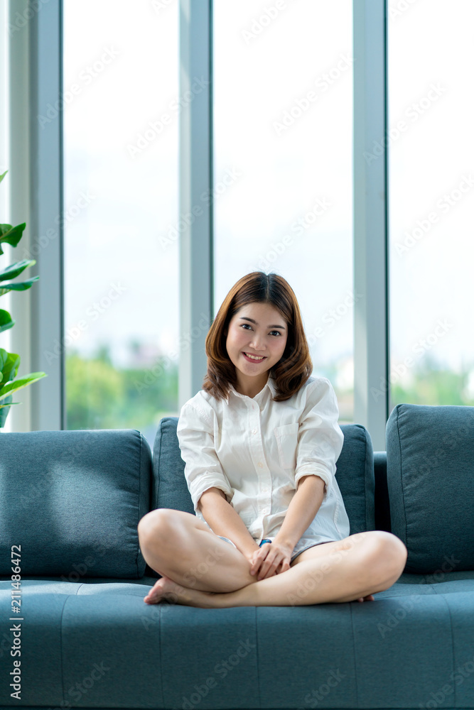 美丽的亚洲迷人女孩在起居区的沙发上微笑和平静的幸福房子概念