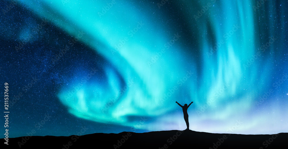 北极光和挪威山丘上举起双臂的站立女子的剪影。极光b