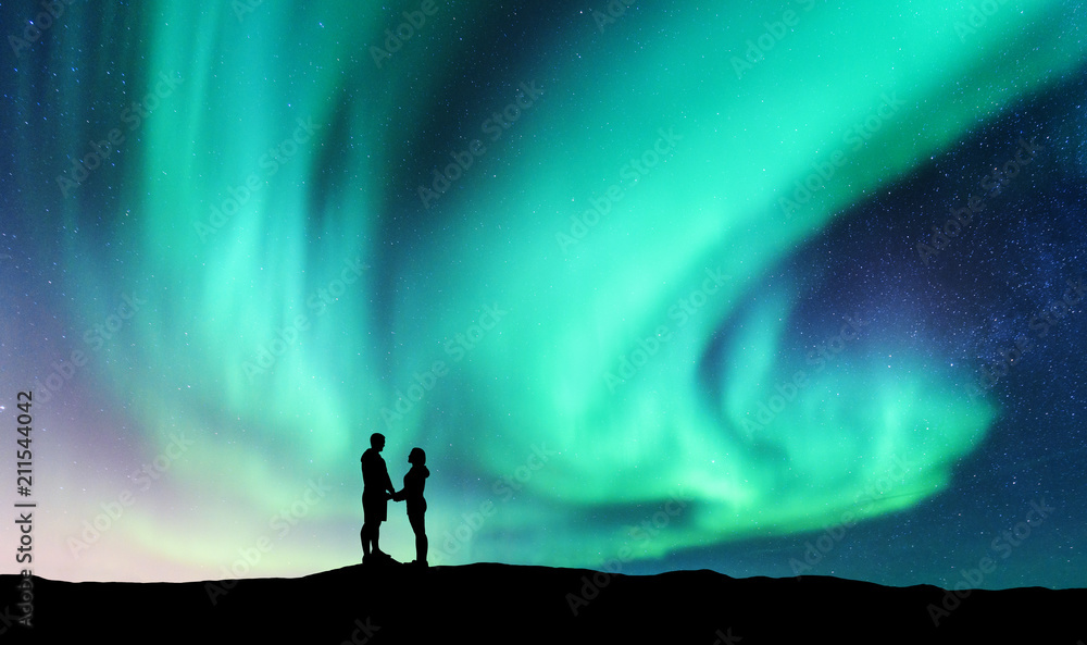 Northern lights and hugging couple on the hill. Landscape with night starry sky, aurora borealis, si