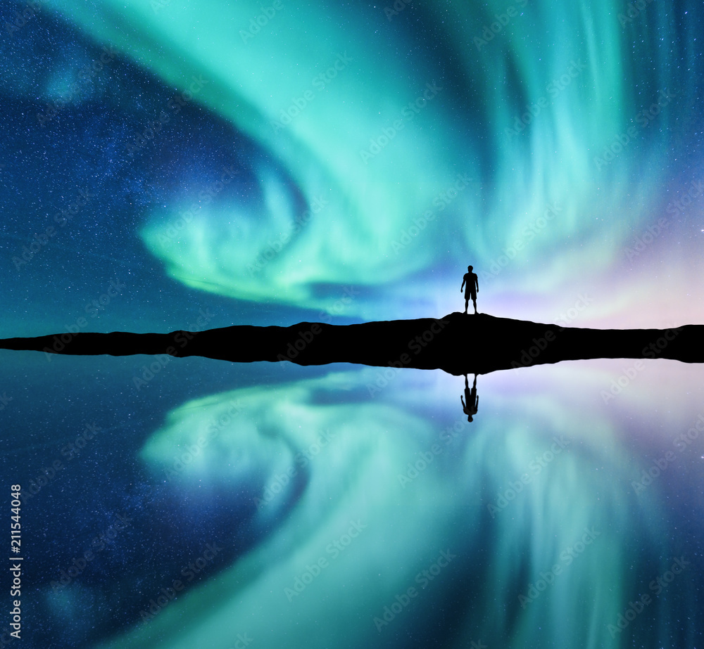 北极光和挪威山丘上站立的人的剪影。北极光和人。星星