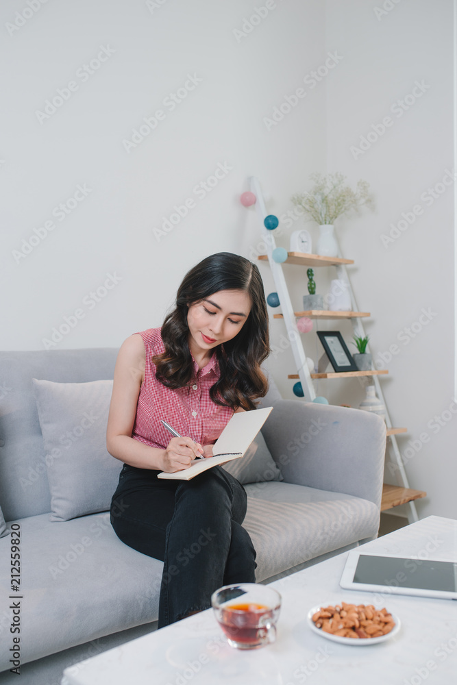 Woman sitting at the table, writing in the notebook and drinking coffee in nice light home interior.