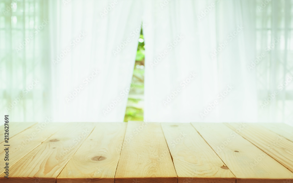 模糊窗帘上的木桌面，从树木花园的背景可以看到绿色的窗户。可以用于