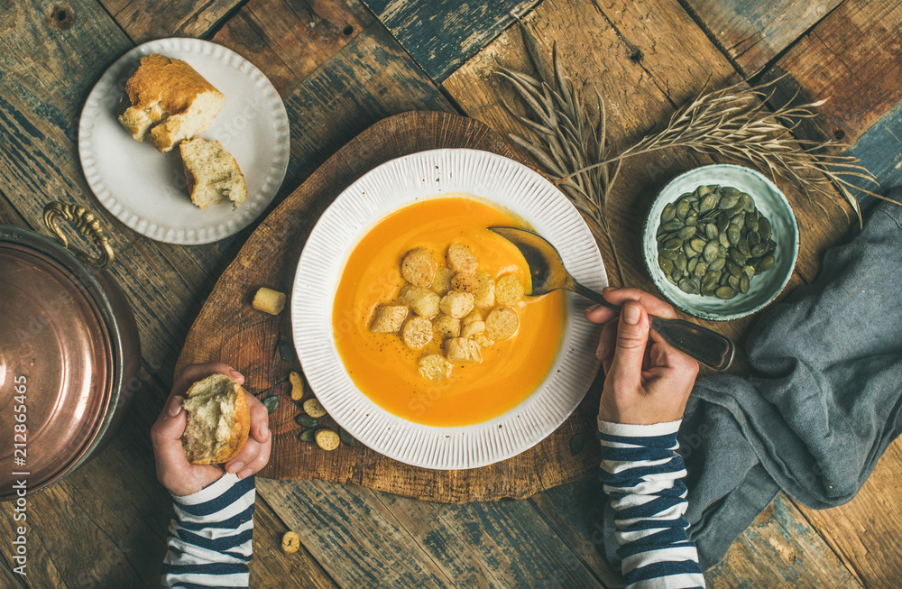 平躺的女性双手和秋天温暖的南瓜奶油汤，盘子里有面包块和种子。
