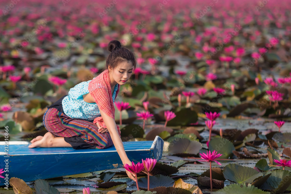 美丽的泰国女士穿着泰式连衣裙在河里抱着莲花。