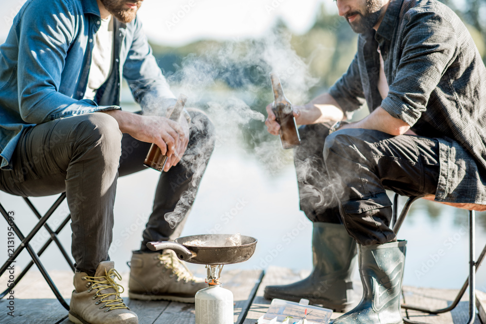 两名渔民在th湖附近的木码头野餐时坐在啤酒里煎鱼