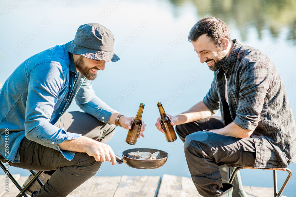 两名渔民在th湖附近的木码头野餐时，坐在啤酒里煎鱼