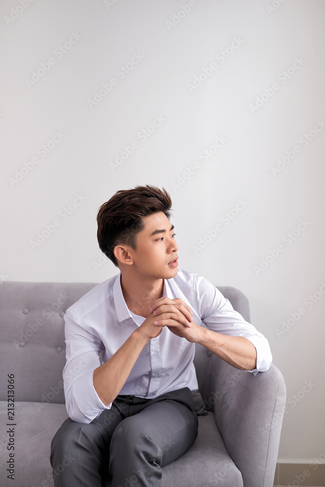 一名年轻的亚洲男子坐在沙发上，看起来在想什么，与世隔绝