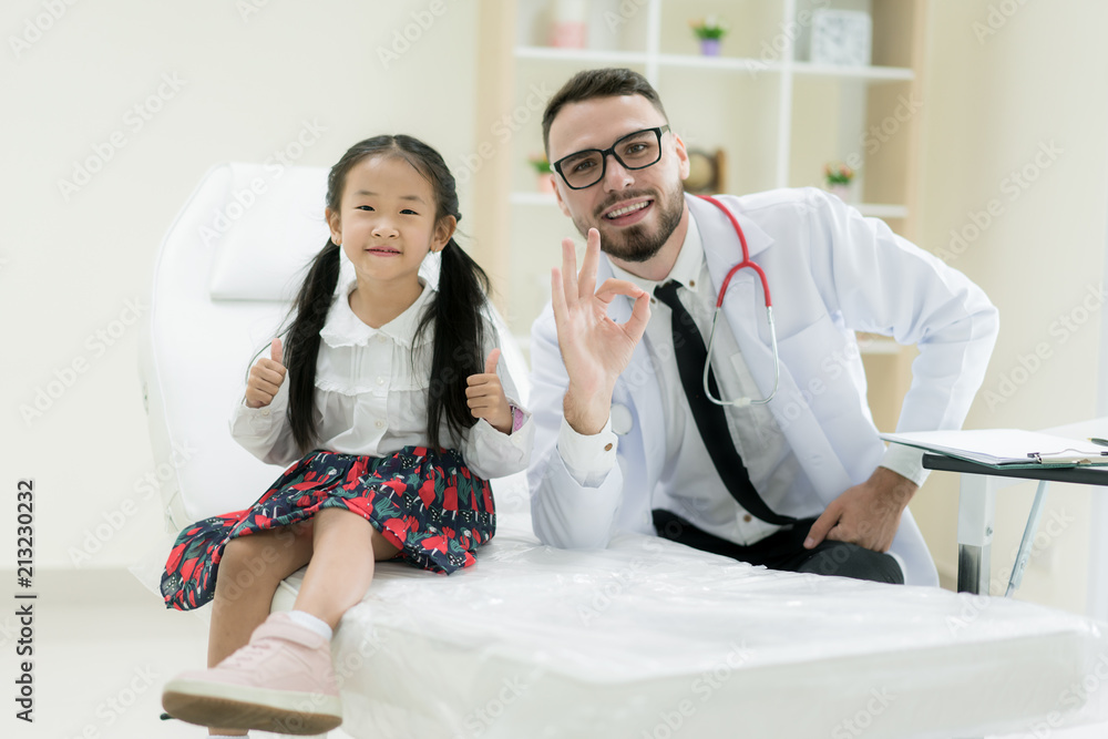 医生带着可爱的小女孩在医院里展示出大大的OK标志。医学和医疗保健概念