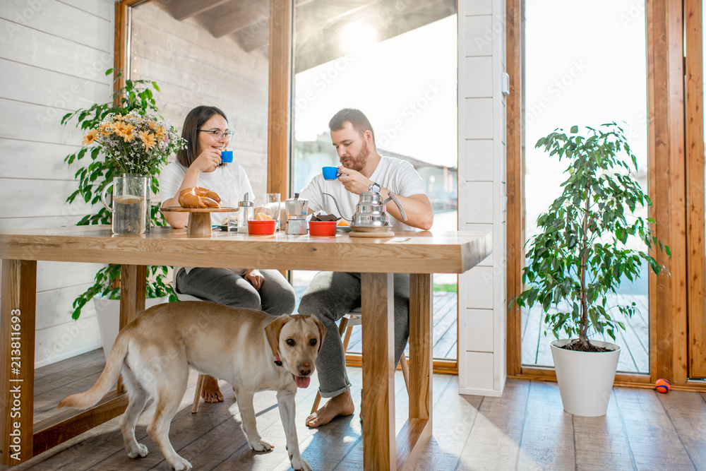 一对年轻夫妇在木屋里和他们的狗坐在桌子旁吃早餐