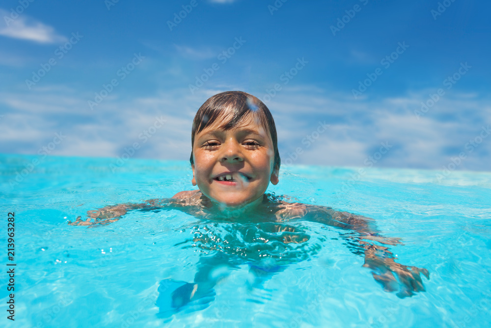 阳光明媚的日子里，爱笑的男孩在室外游泳池游泳