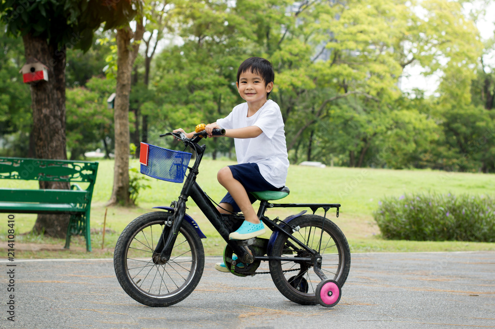亚洲可爱男孩在公园绿色的自然背景下骑自行车。侧视图。