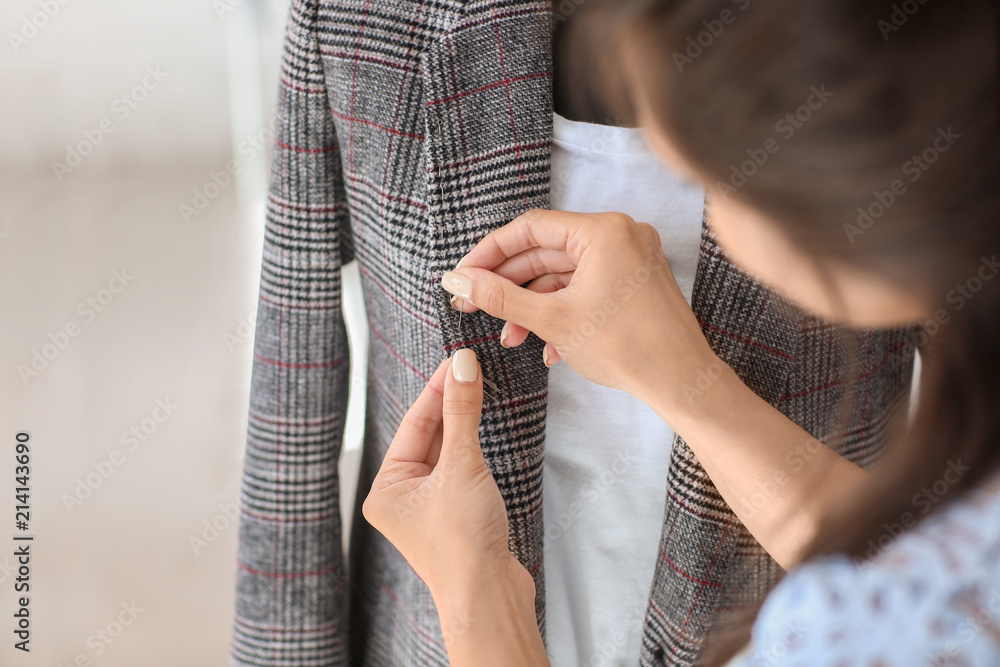 Young female tailor working with jacket in atelier