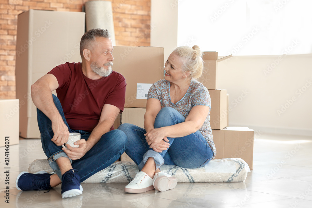 带着移动盒子的成熟夫妇坐在新家的地毯上