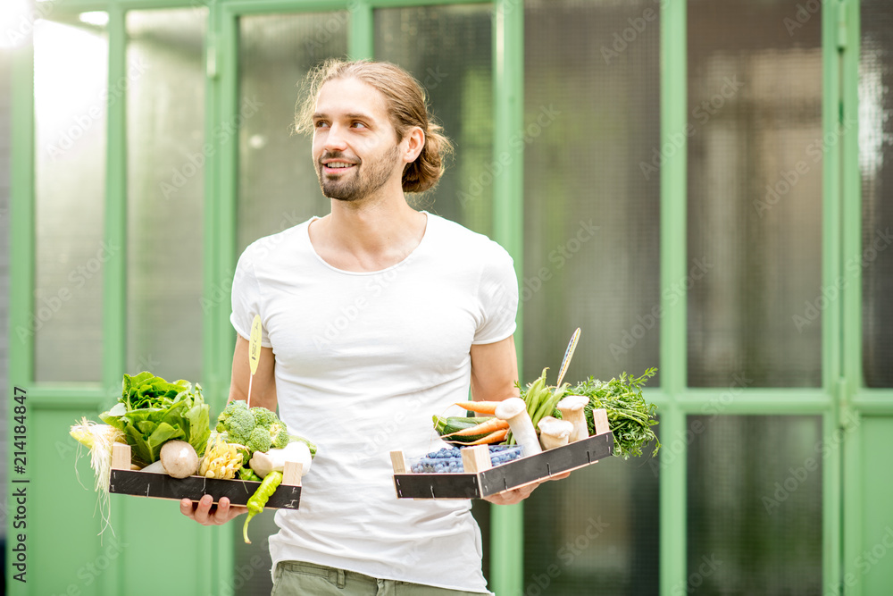 一个英俊男子的画像，他拿着装满新鲜生蔬菜的盒子站在户外的绿色wa上