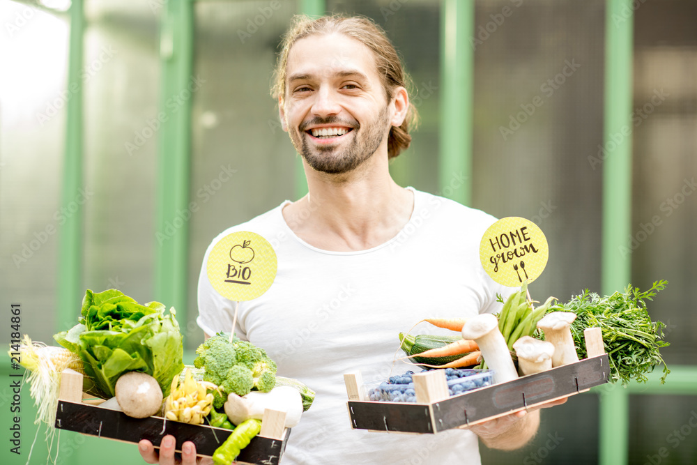 一个英俊的男人的画像，他拿着装满新鲜生蔬菜的盒子站在户外的绿色wa上