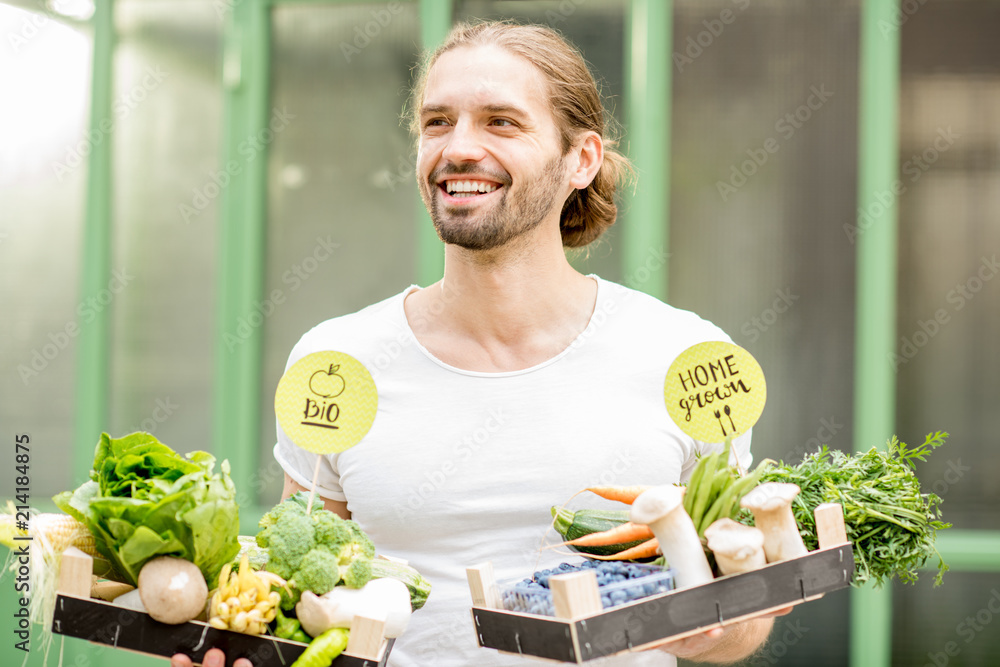 一个英俊的男人的画像，他拿着装满新鲜生蔬菜的盒子站在户外的绿色wa上
