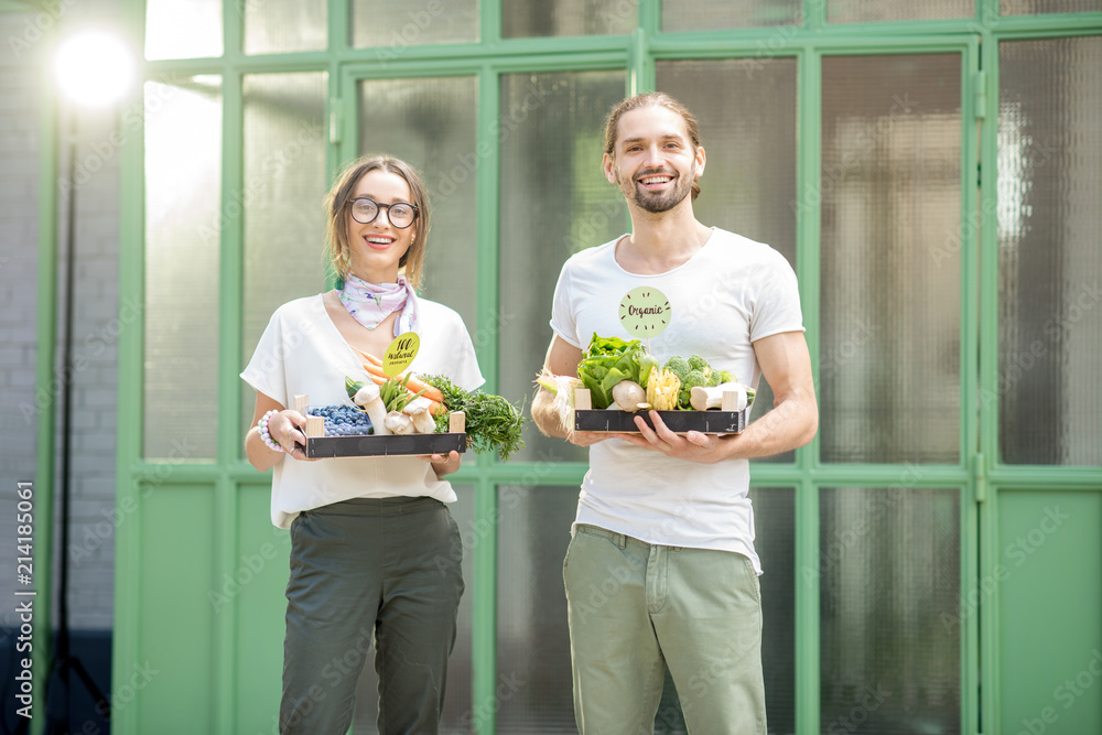 一对幸福的素食夫妇在户外的花架上拿着装满新鲜生蔬菜的盒子的肖像