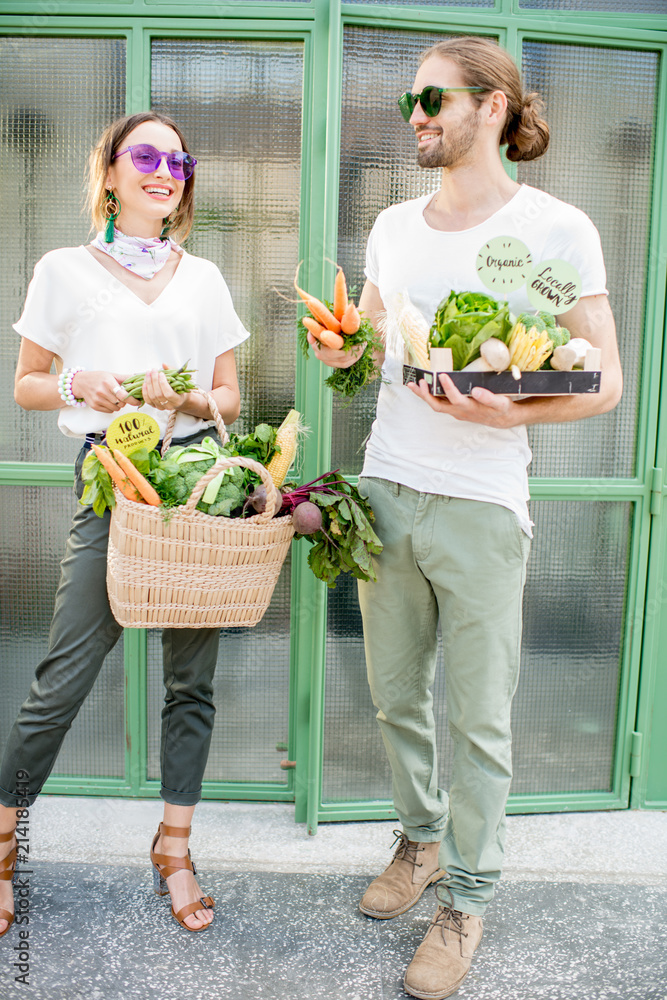 年轻的素食夫妇站在一起，袋子和盒子里装满了当地新鲜的生产品