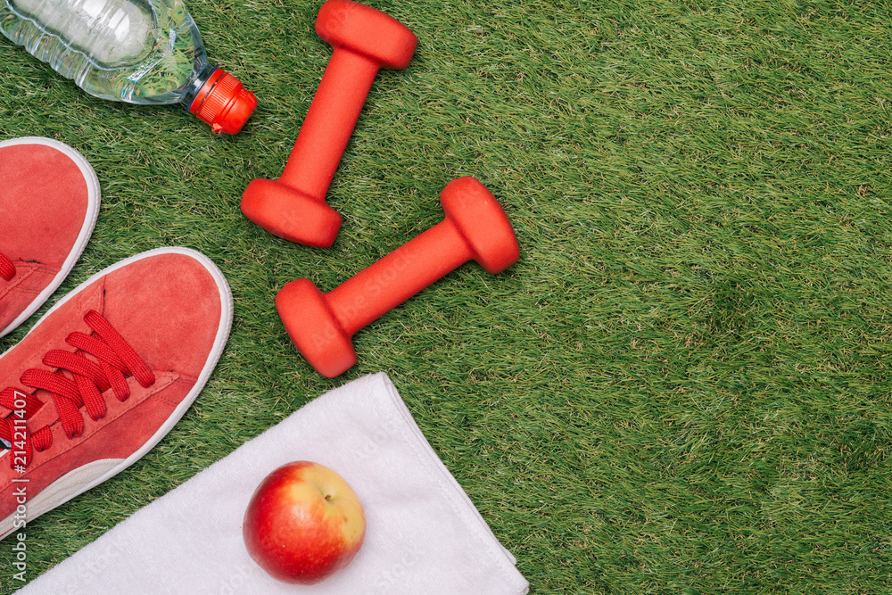 健身概念，包括运动器材、鞋子、苹果、哑铃和绿草上的水。
