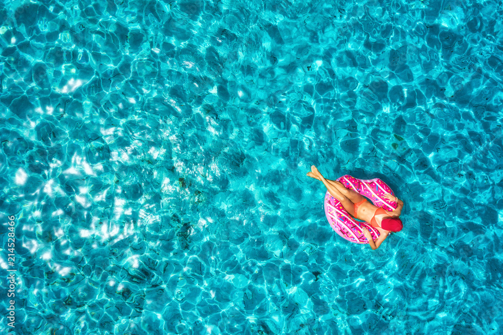 Aerial view of slim young woman swimming on the donut swim ring in the transparent blue sea at brigh