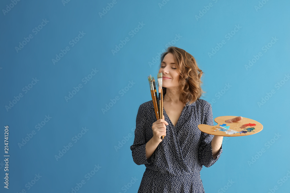 Female artist with brushes and paint palette on color background