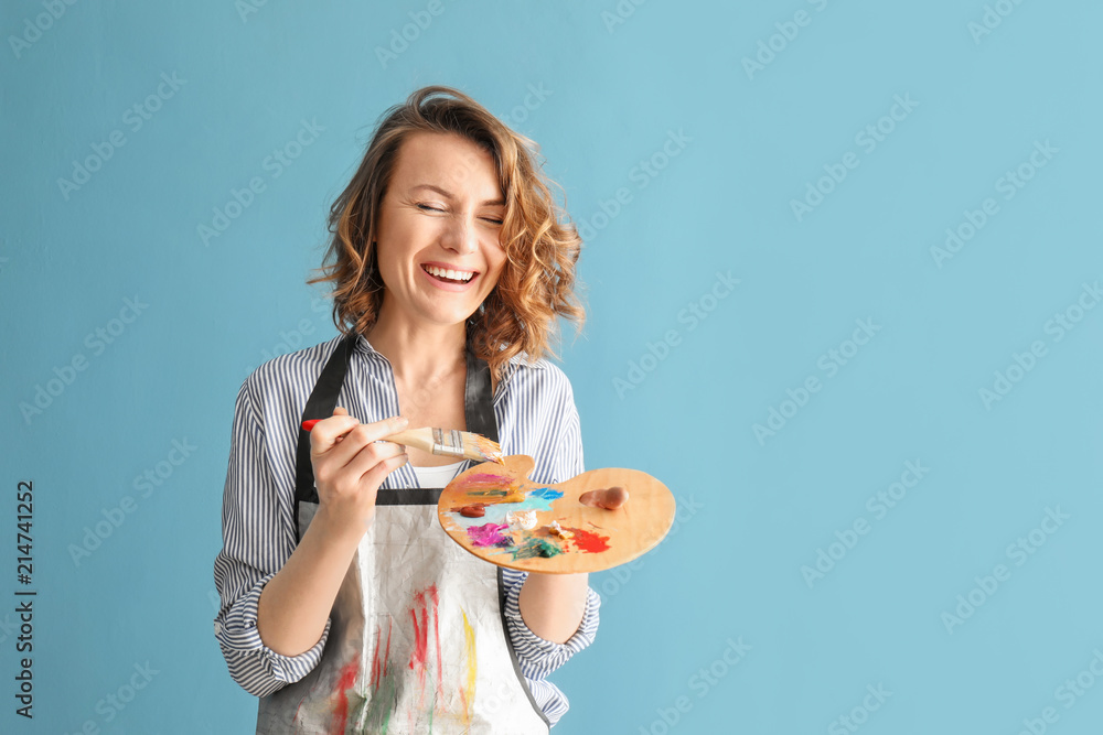 Female artist with brush and paint palette on color background