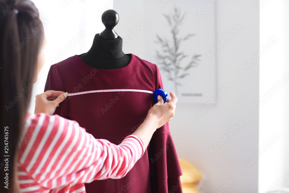年轻的女裁缝在工作室的人体模型上测量衣服