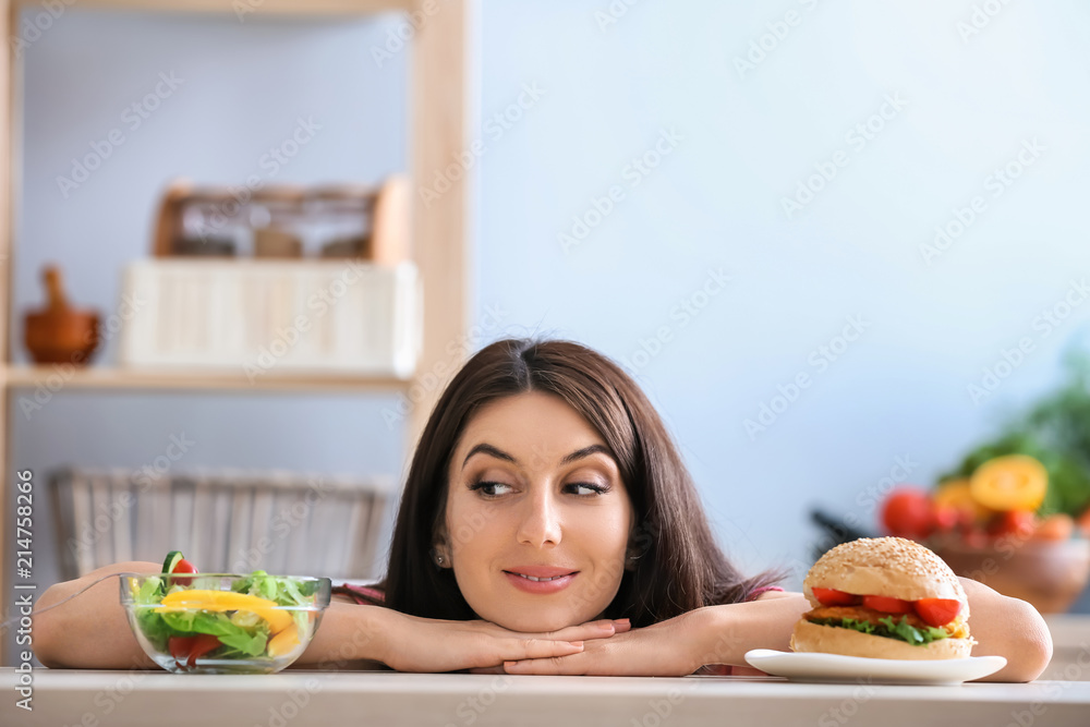 室内有美味汉堡和新鲜沙拉的女人。健康和不健康食物之间的选择