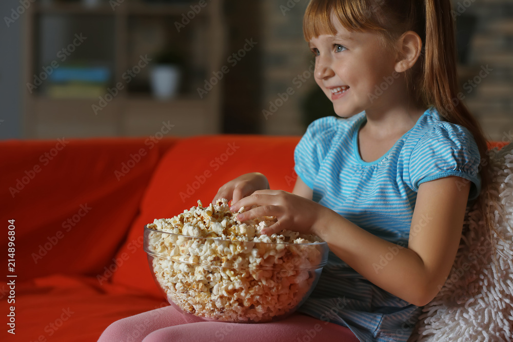 小女孩晚上在沙发上看电视时吃爆米花