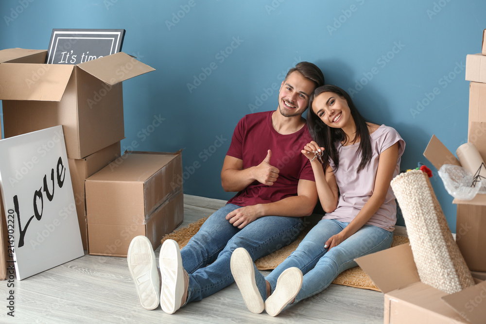 一对年轻幸福的夫妇，带着钥匙和移动的盒子坐在新家的地板上