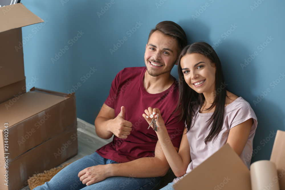 在新家里，带着钥匙和移动箱子的年轻幸福夫妇坐在地板上