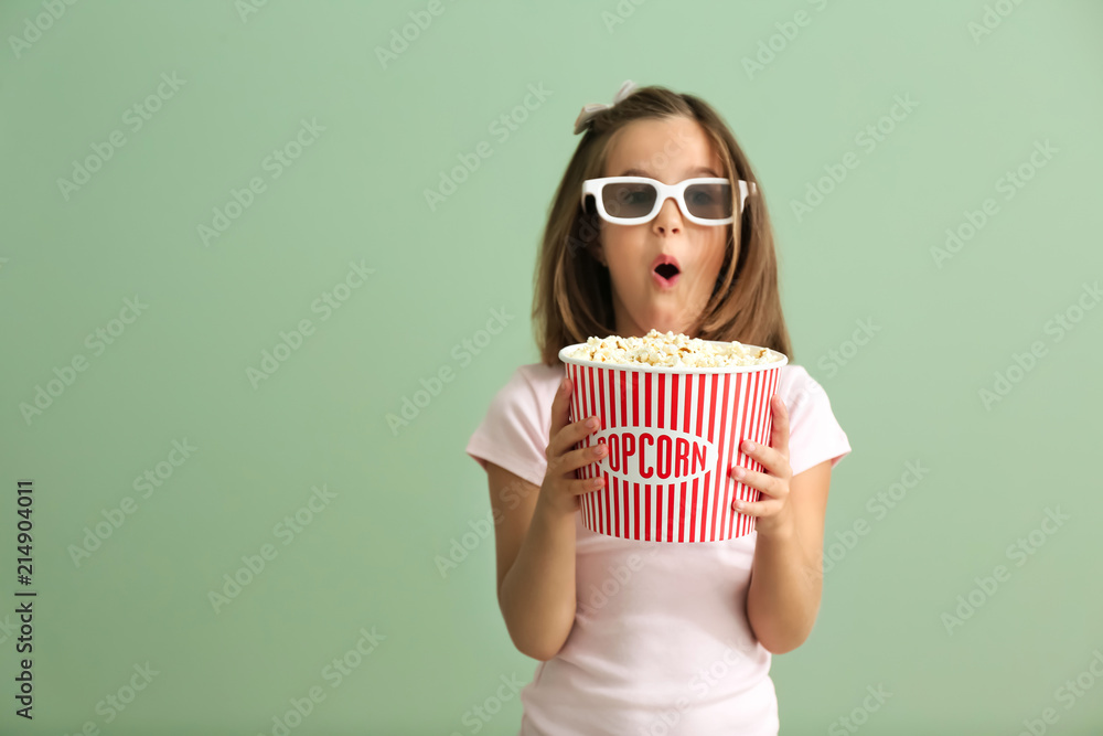 情绪激动的小女孩拿着一杯爆米花在彩色背景下看电影