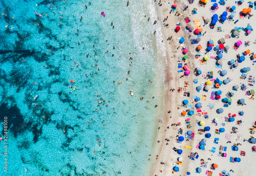 带着彩色雨伞的沙滩鸟瞰图，带着透明蓝色的海湾里游泳的人