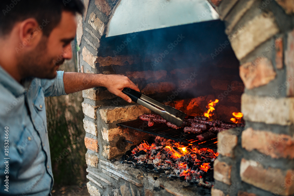 在老式砖砌烧烤上准备肉的英俊男子。
