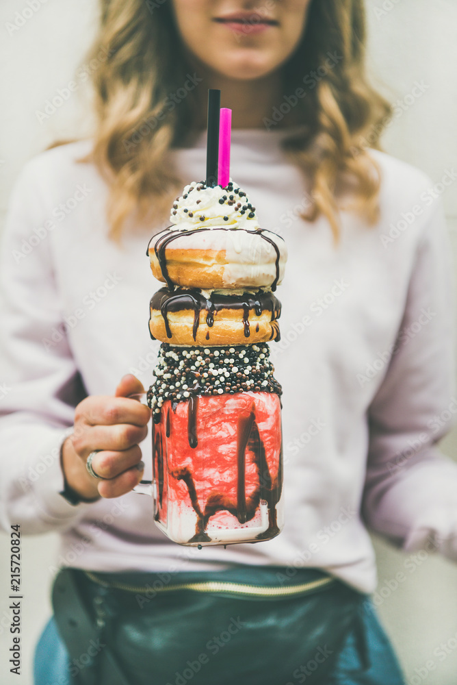 Young woman in light pink clothing holding summer cold strawberry donut freakshake drink with whippe