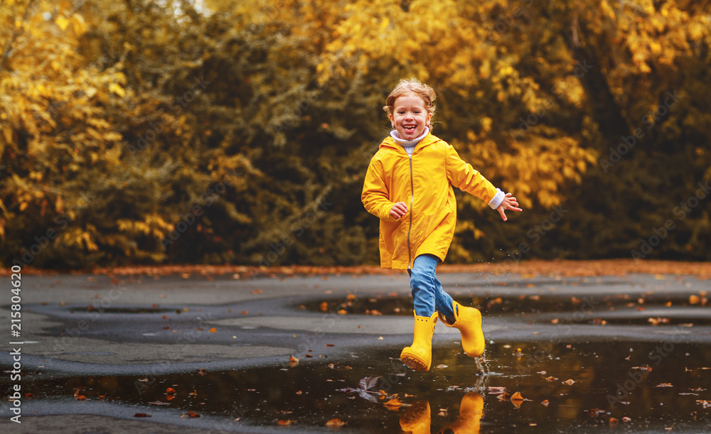 快乐的小女孩，带着雨伞和橡胶靴在水坑里秋天散步