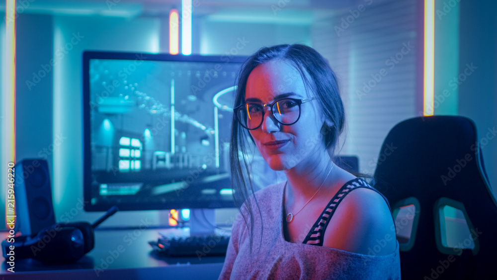 美丽的年轻职业游戏女孩坐在个人电脑前看着相机的肖像