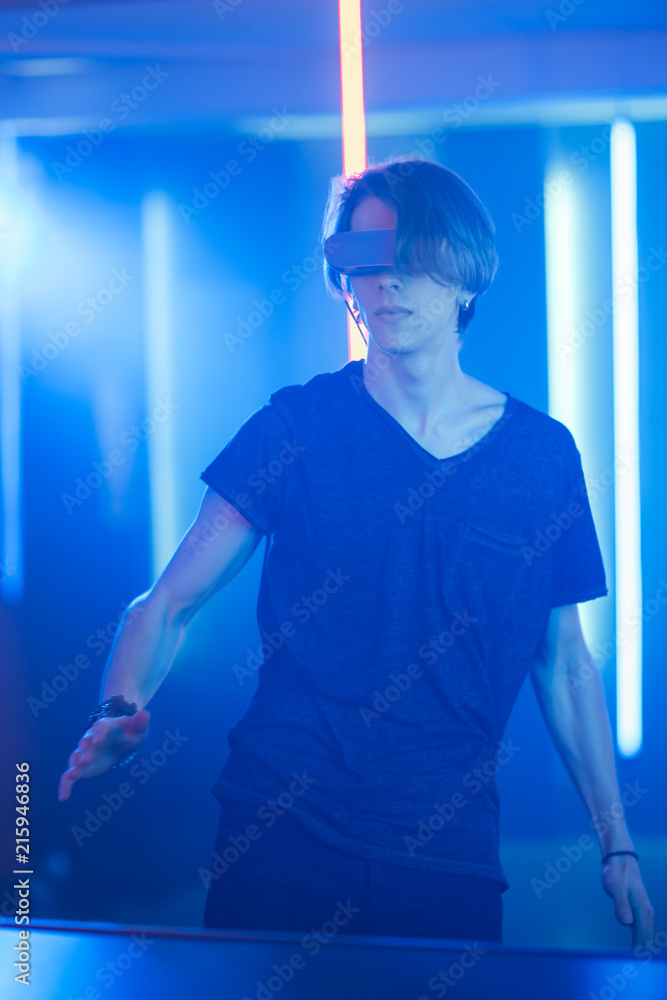 戴着虚拟现实耳机的英俊少年跳舞。背景是炫酷的霓虹复古灯