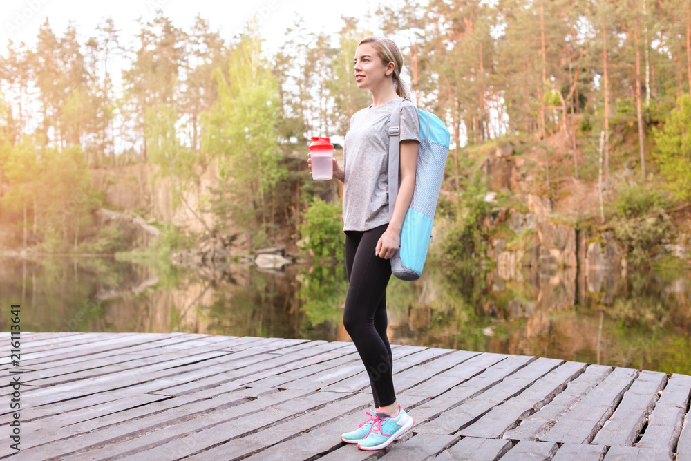 公园里带着瑜伽垫和水瓶的运动型年轻女子