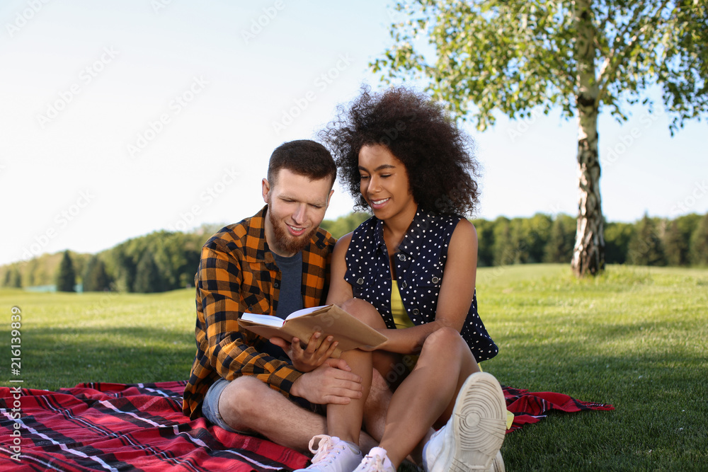 Happy young interracial couple reading book outdoors
