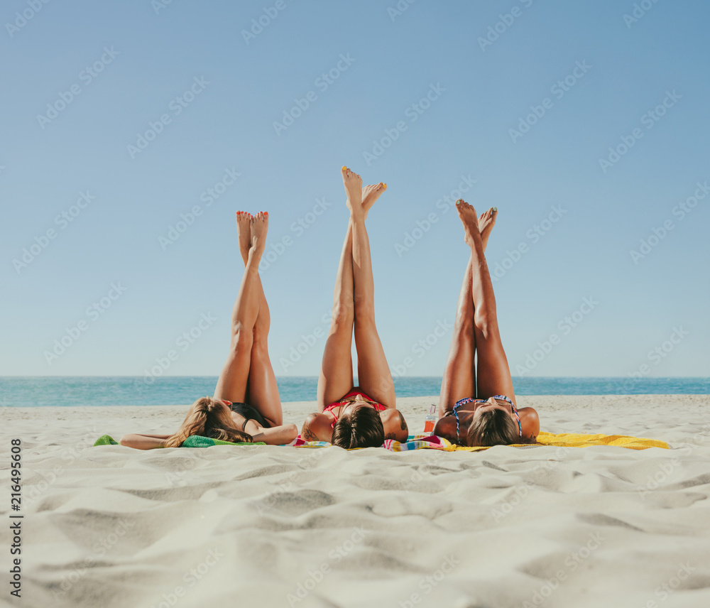 一名身穿比基尼的女子在海滩上晒日光浴，双腿举向天空