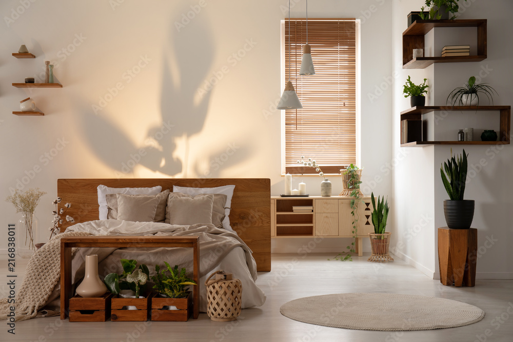 现代卧室内部，床上方的墙上有阴影，有木制架子、盒子和植物。R